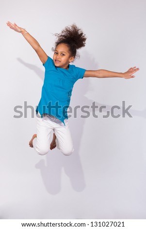 Portrait of cute Young African American girl jumping, over gray background