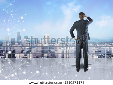 Rear view of businessman standing on skyscraper roof looking at city. Glowing network hologram in the foreground. Toned image double exposure