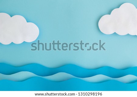 Flat lay of sea waves and clouds made of paper against pastel blue background. Space for copy.