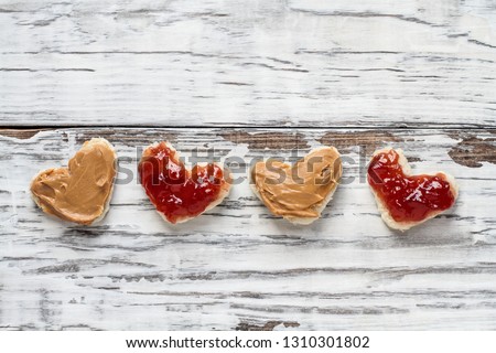 Top view of open face homemade peanut butter and jelly heart shaped sandwiches over a white rustic white wooden table / background. Top view.
