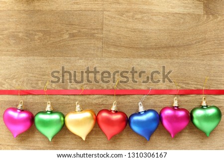 Different coloured hearts hanging from a ribbon against a wooden effect floor background
