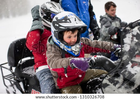 Eager young boy sitting on a snowmobile with his brother in the snow.