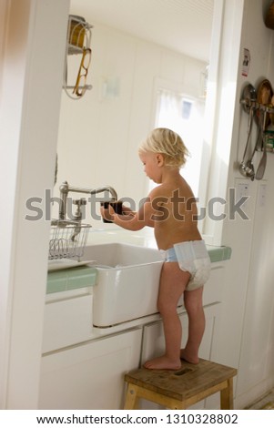 Shirtless young toddler standing at the kitchen sink wearing nappies.
