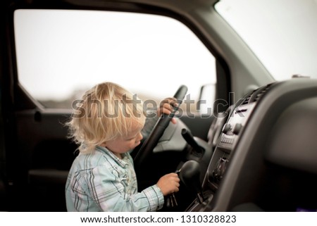 Curious young toddler attempting to put keys into the ignition of a car while sitting in the driver's seat.