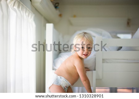 Portrait of a shirtless toddler climbing up to a top bunk bed.