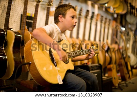 Young boy strumming an acoustic guitar inside a music shop.