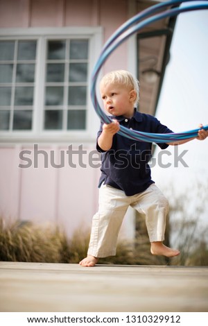 Young boy holding two plastic hoops while standing barefoot outside his home.