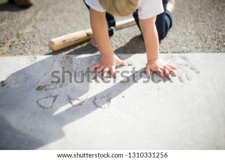 Little boy putting his hand in handprints made in concrete