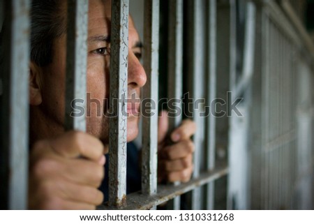 Mature businessman with his head pressed to bars of a cell in a building.