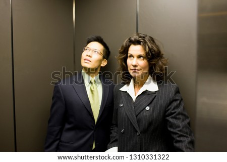 Mid-adult business woman and a young adult male colleague on an elevator.