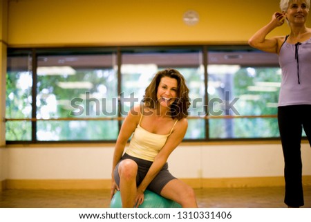 Portrait of a smiling mid-adult woman sitting on an exercise ball inside a studio.