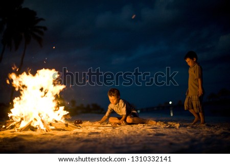 Two boys beside a bonfire on a beach.