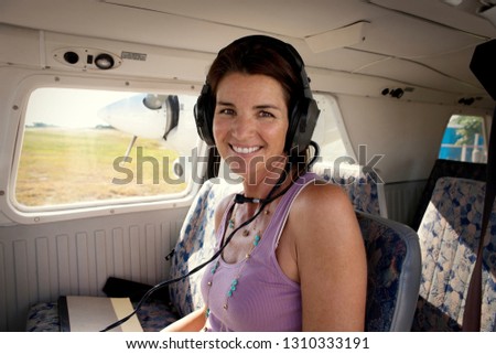 Portrait of a smiling mid-adult woman wearing a headset while sitting inside the cockpit of a small airplane.