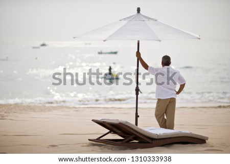 Man standing under sun umbrella looking out at the ocean