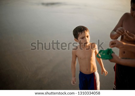 Confused young boy watching his brothers while standing in his swimming costume at the beach.