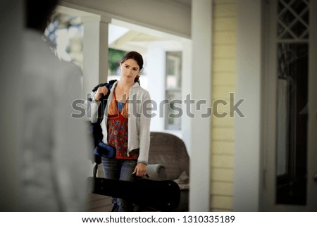 Young woman holding a violin case while arriving on the porch of a house.