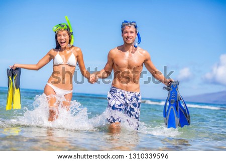 Happy summer fun couple on beach vacation swimming with snorkel equipment running in ocean water. Excited Asian bikini woman and Caucasian man on tropical holidays with flippers and mask.