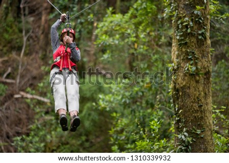 Mid-adult woman moving along a suspended flying fox wire in the forest.