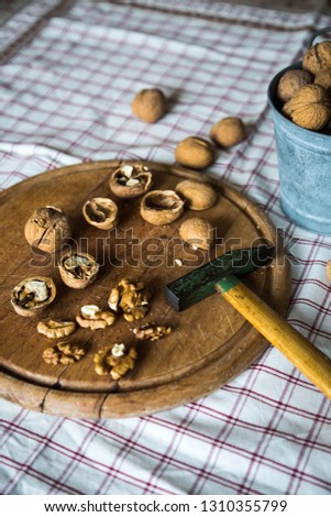 Cracked nuts and hammer on wooden board and vintage metal jar with whole walnuts on background  on checkered tablecloth.