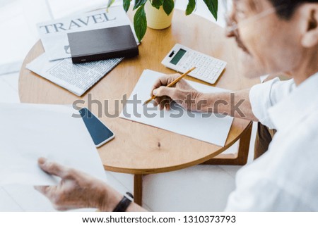 selective focus of retired man holding pencil near paper and smartphone at home