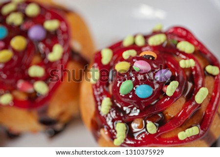 Close-up of garnished muffins with the toppings of sweet candy, jelly and dark chocolate syrup in white plate. 