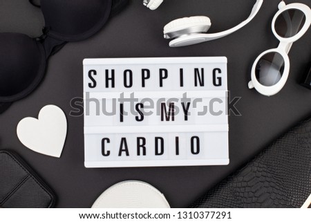 Flat lay with lightbox and funny quote Shopping is my cardio and girls accessories over black background. Girls fashion, shopping, shopaholics concept