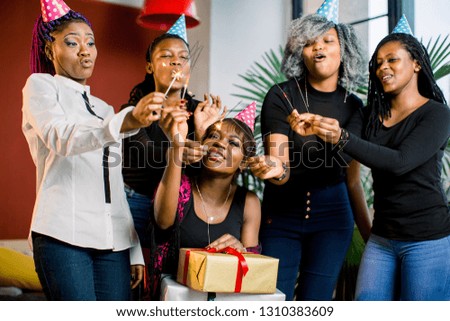 A beautiful smiling African girl holds presents in her hands and celebrates birthday with friends. Girls hold bengal lights in their hands