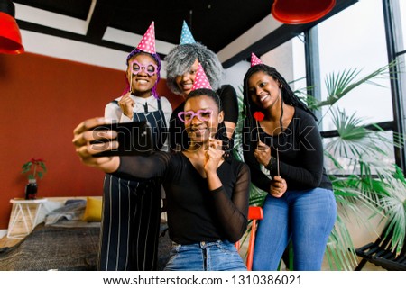 Happy african girls celebrate birthday in hats and take pictures on a smartphone