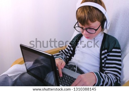 Boy in glasses and earphones is writing on laptop. Online study and learning.