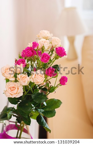 Bouquet of flowers in a room in the interior. Red and white roses in a vase on a table in a bright room. Against the background of the lamps.