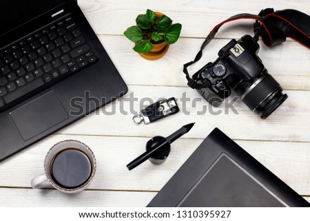 Laptop, digital photo apparatus, drawing tablet, pen, flash, green leaves and coffee cups on old white wooden background
