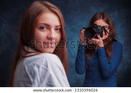 Photo shooting at the studio. Young beautiful female model poses for young woman photographer. Selective focus on photographer.