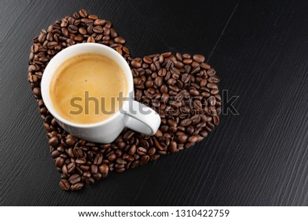 Roasted coffee beans arranged in the shape of a heart on the table. Tasty fragrant coffee in a white mug. Dark background.