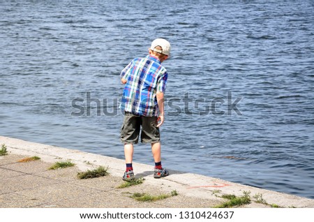 A boy walks on the embankment by the river and takes pictures.