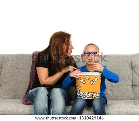 Mother and son sitting on a couch while watching a movie and while eating popcorn against a white background