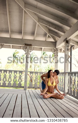 Young woman receives a kiss from her partner while meditating on a beach house balcony.