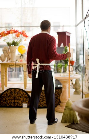 Sales man standing in store holding a broom