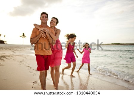 Happy mid-adult couple hugging on a remote sandy beach while out with their two daughters.