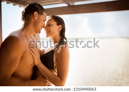 Smiling mid-adult couple hugging on a sandy beach.