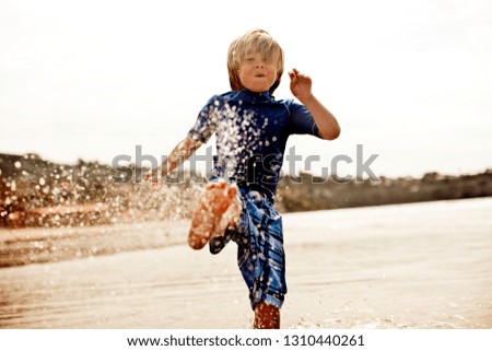 Young boy dressed in blue, splashing in the ocean.