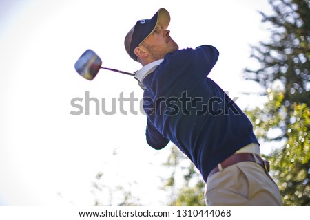 Man swinging a golf club over his shoulder while playing golf on a golf course.