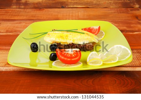 served roast golden fish fillet over wooden table with tomatoes and olives