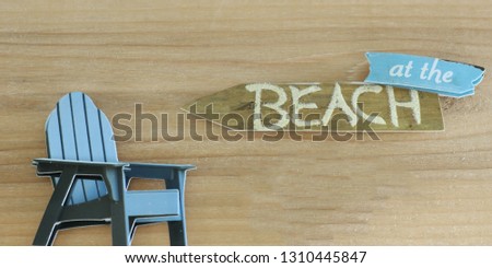 Adirondack chair next to an at the beach sign on a wood background