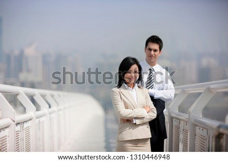 Portrait of two confident business colleagues standing on a footbridge with their arms crossed.