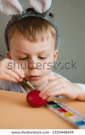 Cute little boy painting easter eggs. He has his ears on his head