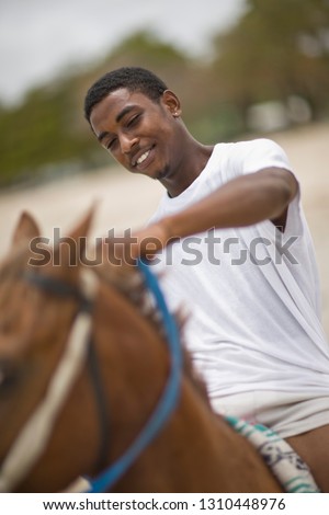 Smiling teenage boy holding the reins while riding a brown horse.