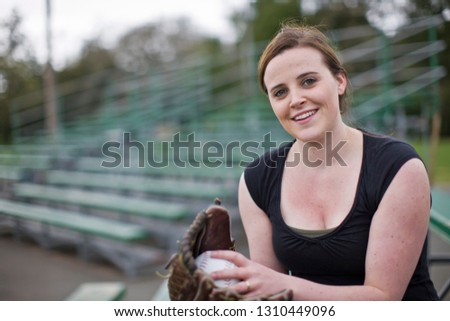 Woman sitting on bleachers holding softball mitt and smiling