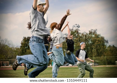 Young adults jumping in the air with their arms raised on a sports field.