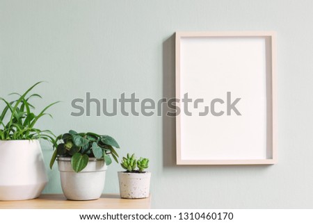 Minimalistic room interior with mock up photo frame on the brown wooden table with beautiful plant in design hipster white pot. Grey walls. Stylish and floral concept of mock up poster frame. 