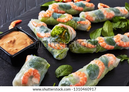 close-up of Fresh Spring Rolls, Vietnamese Rice Paper Rolls with lettuce, bean sprouts, vermicelli noodle, mint and prawns served with peanut dipping sauce on a black slate tray, view from above